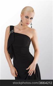 blond attractive young woaman in black dress and black earring looking in camera with strong and sexy eyes posing towards camera while holding while holding her dress