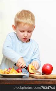 Blond boy child kid preschooler with kitchen knife cutting fruit apple at home. Happy childhood.
