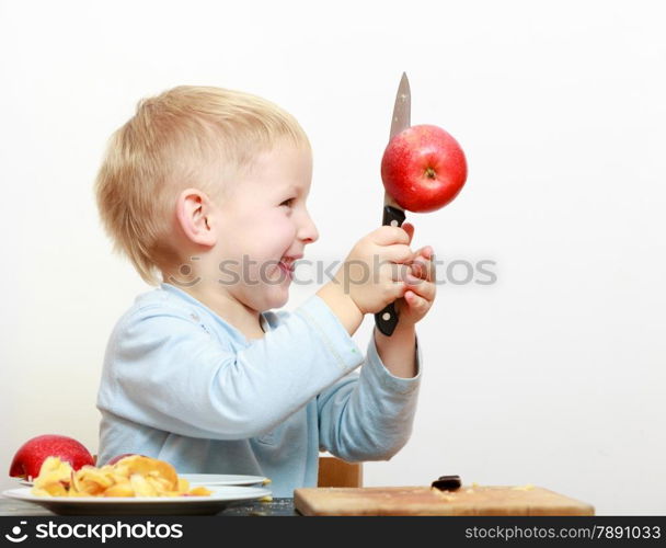 Blond boy child kid preschooler with kitchen knife cutting fruit apple at home. Happy childhood.