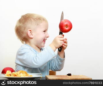 Blond boy child kid preschooler with kitchen knife cutting fruit apple at home. Happy childhood.