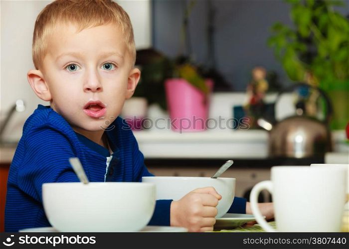 Blond boy kid child eating corn flakes breakfast morning meal at the table. Home.