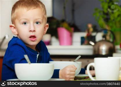 Blond boy kid child eating corn flakes breakfast morning meal at the table. Home.