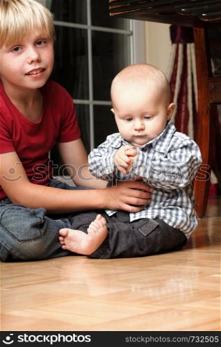 Blond boy with his newborn baby brother indoor