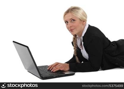 Blond businesswoman laying on front and typing on laptop