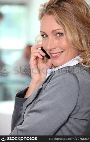 Blond businesswoman taking a call whilst stood in the office