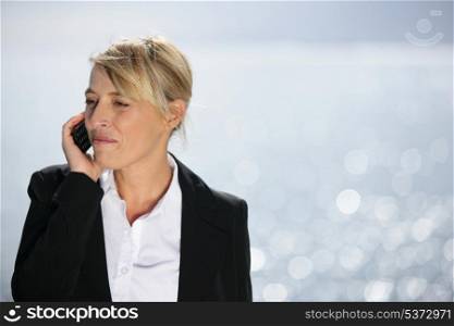 Blond businesswoman taking call by the ocean