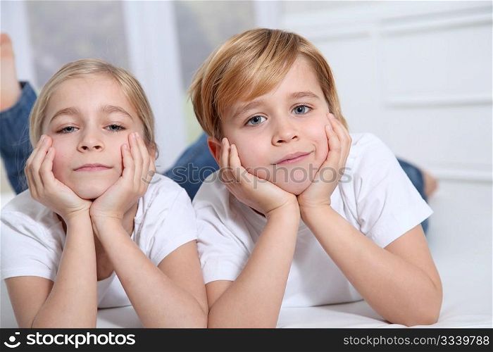 Blond children laying in sofa with hands on chin