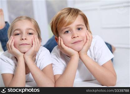 Blond children laying in sofa with hands on chin