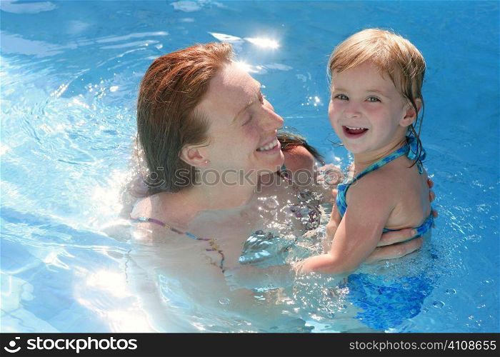 Blond daughter with redhead mother in blue swimming pool