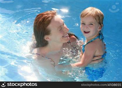 Blond daughter with redhead mother in blue swimming pool