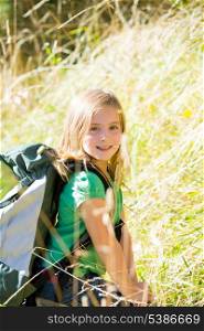 Blond explorer kid girl walking with backpack between forest grass