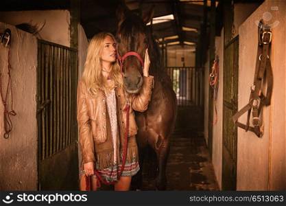 Blond girl holding horse at stable. Blond girl holding horse at stable corridor