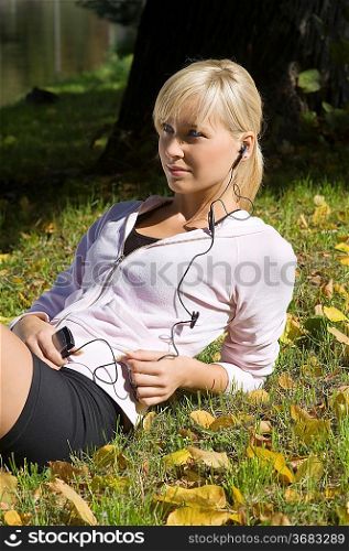 blond girl laying down on grass listening music