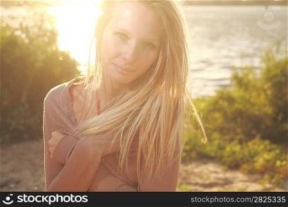 blond girl sitting near river against sun