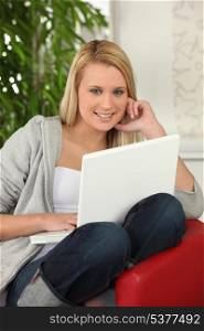 Blond girl with laptop computer sitting on a sofa