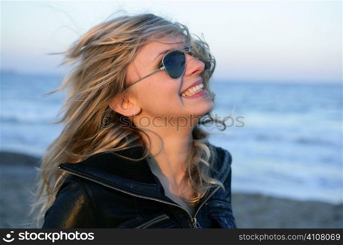 Blond girl with retro sunglasses on the blue beach, wind