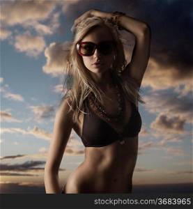 blond girl with sunglasses posing and drinking in a dark and contrast portrait