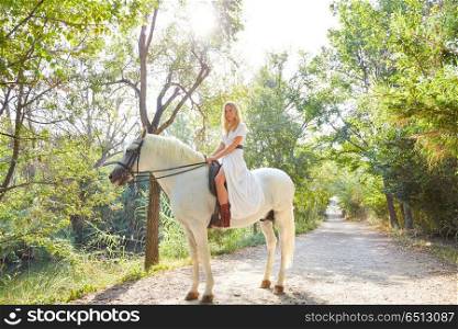 Blond girl woman riding a white horse in track. Blond girl woman riding a white horse in a forest track outdoor