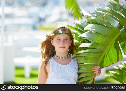 Blond kid girl at banana tree leaves in bright day light in Mediterranean