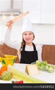 Blond kid girl junior chef on countertop funny gesture with roller knead
