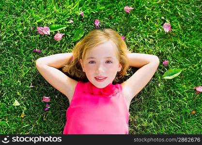 Blond kid girl lying on garden grass smiling happy aerial view