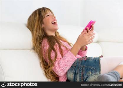 Blond kid girl playing fun with mobile smartphone on white sofa byod