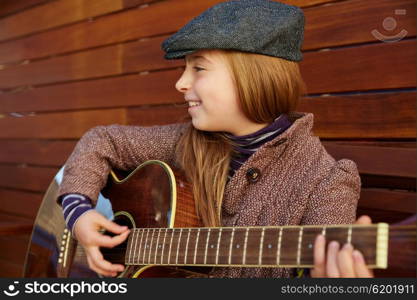 blond kid girl playing guitar with winter beret and coat on wooden background