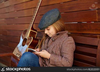 blond kid girl playing guitar with winter beret and coat on wooden background