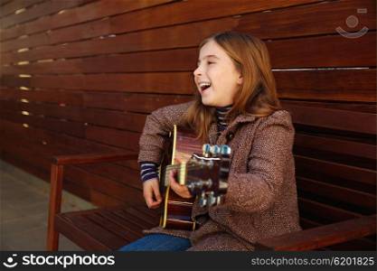 blond kid girl playing guitar with winter coat on wooden background