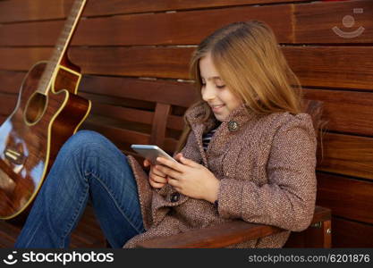 blond kid girl playing smartphone and guitar on wooden background