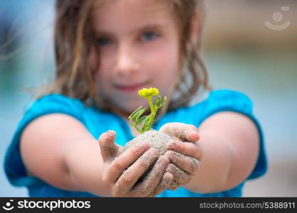Blond kid girl showing a beach plant with sand in her hands selective focus