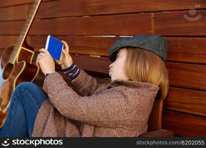 blond kid girl taking selfie with guitar and winter beret and coat on wooden background