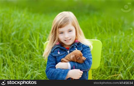Blond kid girl with puppy pet dog sit in outdoor green grass
