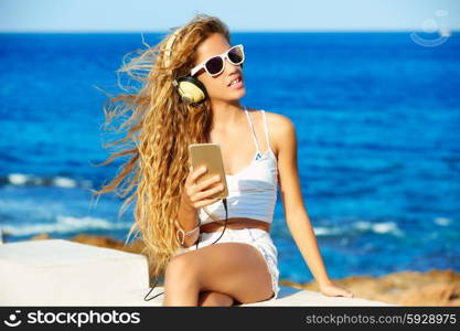 Blond kid teen girl hearing headphones music on smartphone in a beach