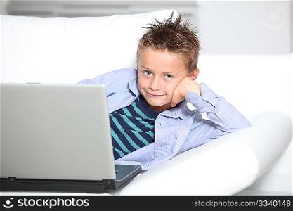 Blond little boy sitting on sofa with laptop computer