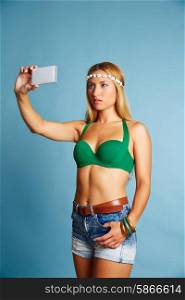 Blond long hair girl with jeans shorts selfie photo with smartphone on blue background