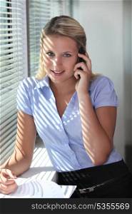 Blond office worker making telephone call whilst stood by window