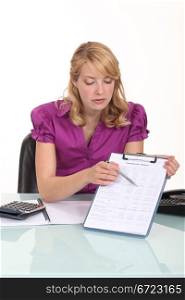 Blond office worker pointing at clip-board with pen