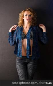 blond sexy girl with curly hair in blue swowing her bra standing against a black wall