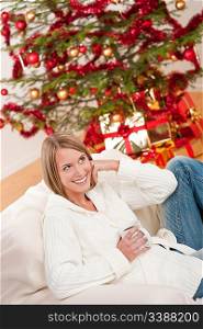 Blond smiling woman with cup of coffee in front of Christmas tree