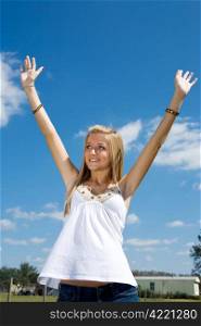Blond teen girl outdoors raising her arms in praise.