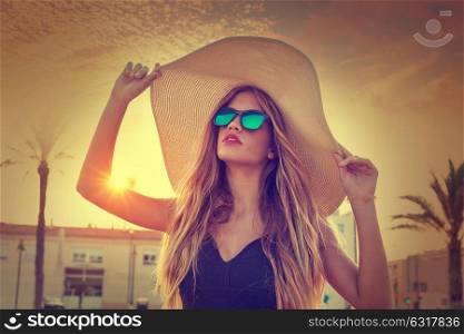 Blond teen girl sunglasses and pamela sun hat at palm tree sunset filtered image