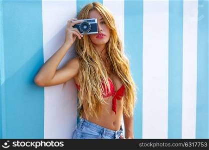 Blond teen summer girl with vintage photo camera in blue stripes wall background