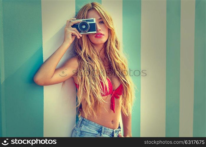 Blond teen summer girl with vintage photo camera in blue stripes wall background filtered image