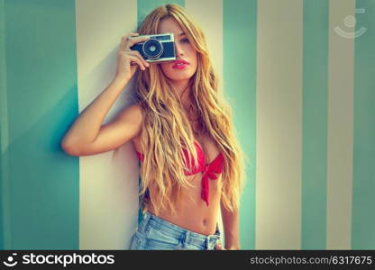 Blond teen summer girl with vintage photo camera in blue stripes wall background filtered image