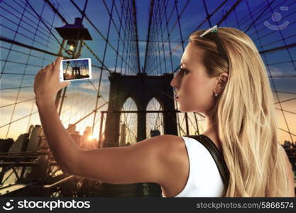 Blond tourist girl taking photo in Brooklyn Bridge New York at sunset Photomount