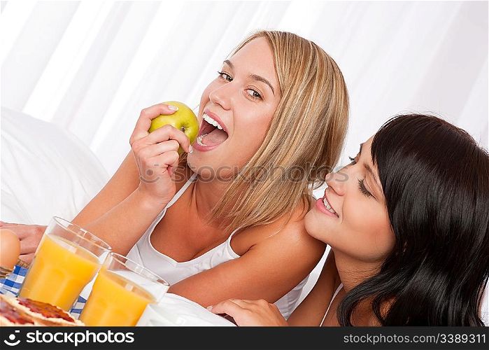 Blond woman and brunette having breakfast in bed