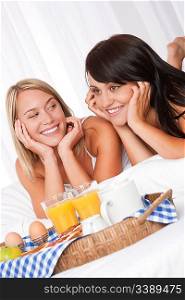 Blond woman and brunette having breakfast together in white bed