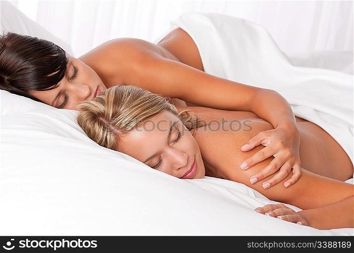 Blond woman and brunette lying down in white bed and sleeping naked together