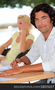 Blond woman and dark haired man sat outdoors with coffee